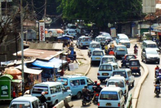 Sky blue angkot minivans causing traffic jam as some stop in the middle of the road to pick up or drop off passengers.