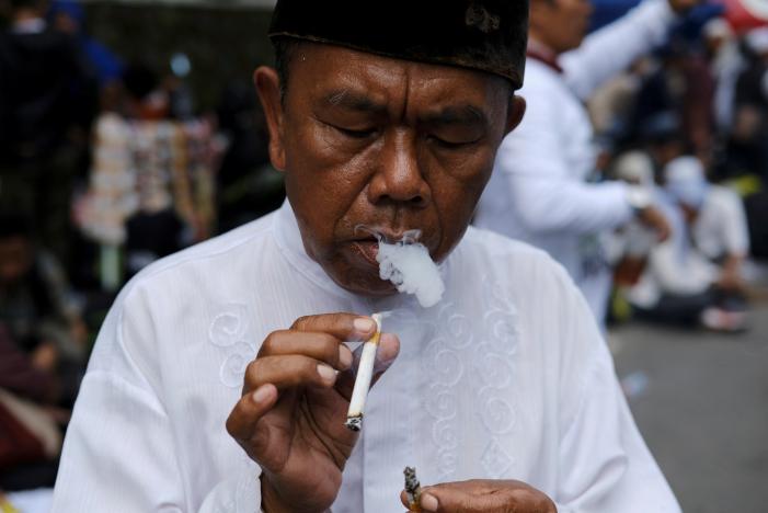 An Indonesian man smokes a cigarette during a protest near South Jakarta court in Jakarta, Indonesia, May 9, 2017. Picture taken May 9, 2017. REUTERS/Beawiharta