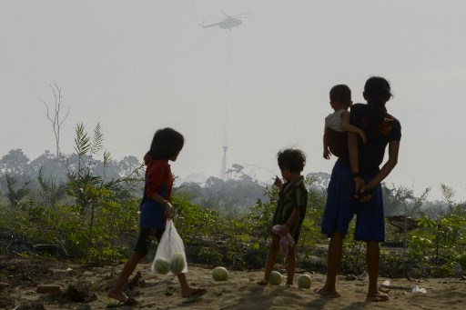Acehnese villagers watch as a helicopter drops water over a peat forest fire in Meulaboh, Aceh province on July 26, 2017.
Some 35 fire hotspots in the past week have destroyed 70 hectares (0.27 square miles) of forests and other land in Aceh, the national disaster agency said. The haze is an annual problem in Indonesia caused by fires set in forest and on carbon-rich peatland in Indonesia to clear land for palm oil and pulpwood plantations.  / AFP PHOTO / CHAIDEER MAHYUDDIN