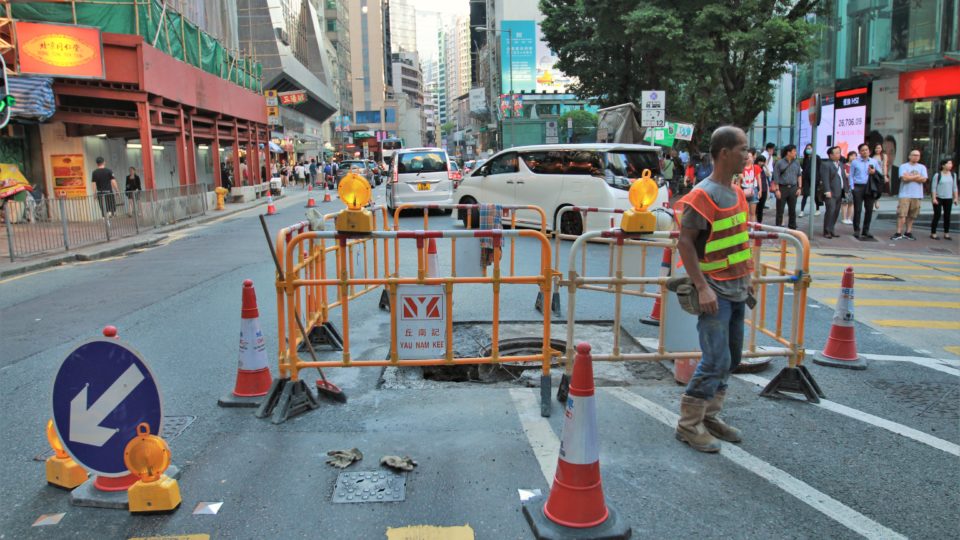 A construction worker stands by the hole on Queen’s Road Central, one of the busiest thoroughfares in Hong Kong. Photo: Cecilia Wong/Coconuts Media