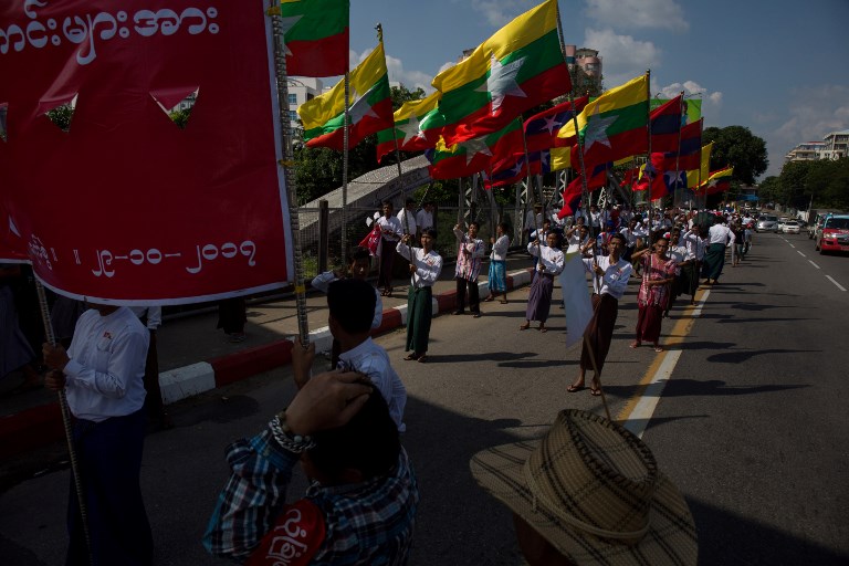 Men carry the national flags from Myanmar high as they march in an avenue in Yangon on October 29, 2017. / AFP PHOTO / Paing Aung