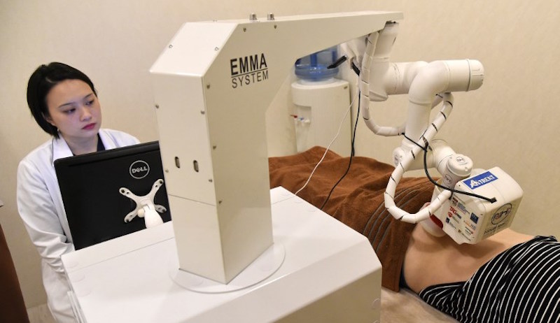 Singaporean physician Calista Lim Hui Min (L) monitors progress as a robot masseuse named Emma massages patient Elaine Low, 35, at the NovaHealth traditional Chinese medicine (TCM) clinic in Singapore. Photo: Roslan Rahman/AFP