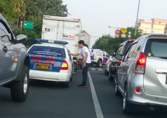 A man returning a plastic cup that was thrown out of a police car in Jakarta. Photo: Video screengrab