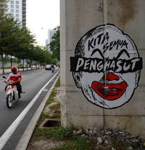 (FILES) This file photo taken on March 21, 2016 shows a motorcyclist riding past a poster depicting a clown-faced caricature of Malaysian Prime Minister Najib Razak in Kuala Lumpur.
A Malaysian artist was jailed for a month on February 20, 2018 for publishing a caricature of Prime Minister Najib Razak looking like a clown, the latest government critic to be imprisoned. / AFP PHOTO / Mohd RASFAN