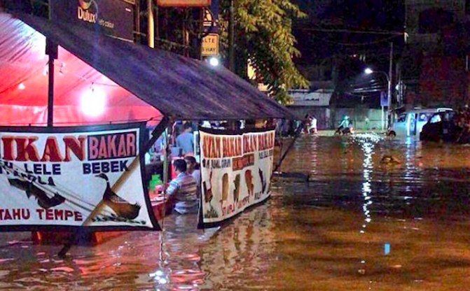 A viral photo showing a Jakarta resident eating at a warung despite being waist-deep in flood water. Photo: Instagram/@tmcpoldametro