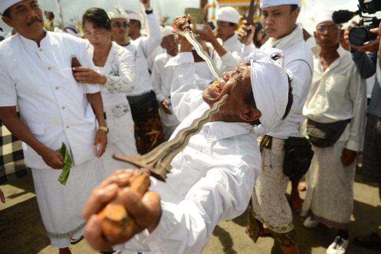 A Balinese man in a trance holds daggers to his cheeks during a Melasti ceremony prayer at Petitenget beach near Denpasar on Indonesia’s resort island of Bali on March 14, 2018. 
Melasti is a purification festival which is held several days before “Nyepi”, the day of silence, when Hindus on the island of Bali are not allowed to work, travel or take part in any indulgence. The Indonesian holiday island of Bali shuts down for the day of silence to mark the Hindu new year on March 17. Photo: Sonny Tumbelaka/AFP