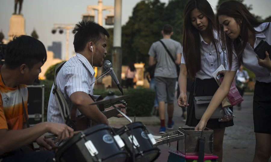 This photo taken on Jan. 11, 2018 shows two university students donating money to blind singer Singhkum Boonriang, 28, as he performs with his guitar at Lumpini park. Photo: Lillian Suwanrumpha/ AFP