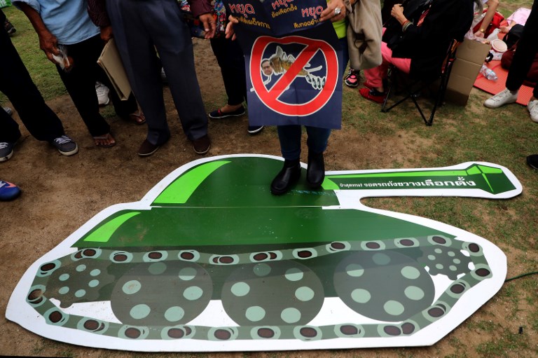 A Thai anti-junta activist holds a banner saying stop prolonging power, stop delaying elections while stepping on a cartoon of a military tank during a pro-democracy rally at a university field in Bangkok on March 10, 2018. AFP PHOTO / Pattarachai Preechapanich 