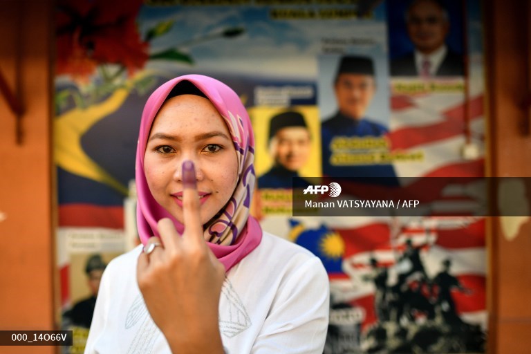A Malaysian woman poses with her inked finger after casting her vote during the 14th general election, in front of posters of former prime minister Mahathir Mohamad and current prime mister Najib Razak, at a polling station in Kuala Lumpur on May 9, 2018. Manan Vatsyayana / AFP