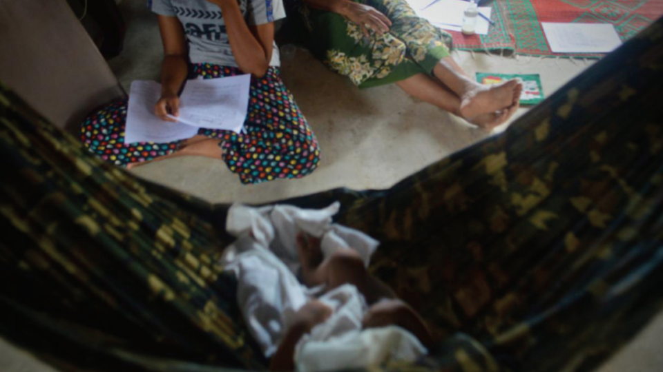 The baby of undocumented Burmese Muslim parents naps in a hammock while relatives sit nearby. Photo: BHRN