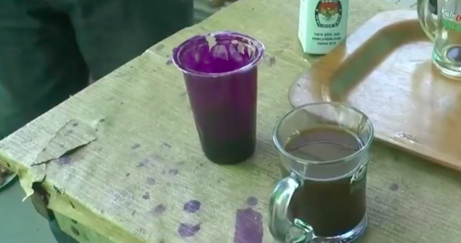 Purple election ink in cup placed next to cup of coffee. Photo: Youtube/CNN Indonesia