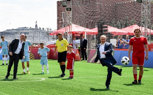 Russia’s President Vladimir Putin (2nd R) kicks a ball as FIFA President Gianni Infantino (L) watches as they take part in the opening of an exhibition soccer match at the World Cup Football Park on the Red Square in Moscow on June 28, 2018. / AFP / Yuri Kadobnov 