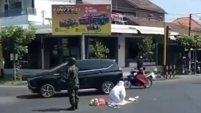 A woman praying in the middle of the road in Indonesia while a soldier stands guard. Photo: Facebook