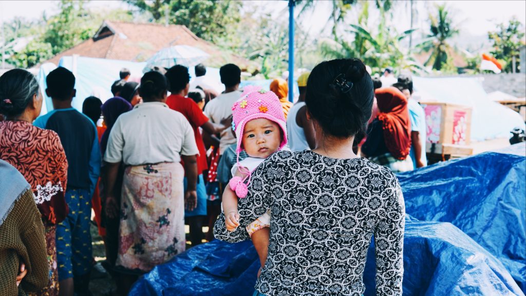 A mother waits in line with her baby as provisions are handed out in their evacuation post in West Lombok. Photo: Coconuts Bali