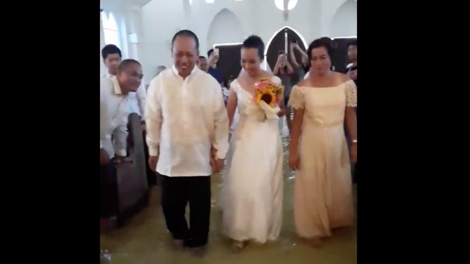 Bride Jobel Delos Angeles walks down the flooded aisle with her parents on her wedding day. 
