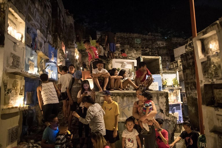 People sit atop of apartment type tombs while visiting their loved ones at Barangka cemetery in Marikina, east of Manila on November 1, 2018. – Millions packed cemeteries across the heavily Catholic Philippines on Thursday, for traditional remembrances of the dead that mix somber reflection and the nation’s penchant for festivity. (Photo by NOEL CELIS / AFP)