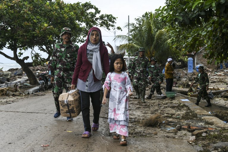 A mother walks with her daughter near an area of collapsed houses in Rajabasa in Lampung province on December 25, 2018, three days after a tsunami – caused by activity at a volcano known as the “child” of Krakatoa – hit the west coast of Indonesia’s Java island. – Desperately needed aid flowed into a stretch of Indonesia’s tsunami-struck coastline on December 25, officials said, but aid workers warned that clean water and medicine supplies were dwindling as thousands crammed makeshift evacuation centres. (Photo by Mohd RASFAN / AFP)