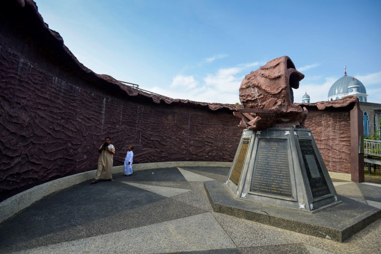 Boys walk in front of a landmark dedicated to the 2004 Boxing Day tsunami, which devastated Aceh province 14 years ago, in Banda Aceh on December 26, 2018. – The 2004 Boxing Day tsunami was one of the deadliest disasters in history, and left some 220,000 people dead in countries around the Indian Ocean, including some 168,000 Indonesians. (Photo by Chaideer MAHYUDDIN / AFP)