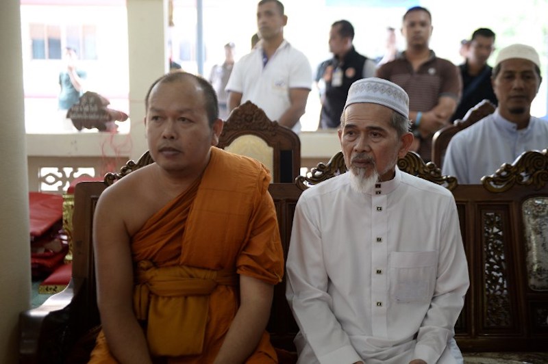 A Buddhist monk and a Muslim village leader sit together to express sympathy and support during a gathering in Rattanaupap temple in Narathiwat province on January 19, 2019 following an attack by black-clad gunmen that killed two Buddhist monks. (Photo by Madaree TOHLALA / AFP)