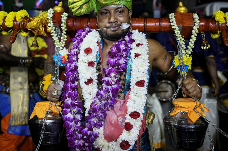 This picture taken on January 20, 2019 shows Kumaraguru Kunalan, 38, making his religious pilgrimage to a Batu Caves temple by carrying “kavadi” offerings on his shoulders with his tongue pierced with a steel skewer during Thaipusam festival celebrations at a complex of temples outside Kuala Lumpur. – Malaysian Hindu devotee Kumaraguru Kunalan hauled a wooden pole with metal pots hanging from it up to a temple carved into a hillside as drumming and incense smoke filled the air. (Photo by MOHD RASFAN / AFP)