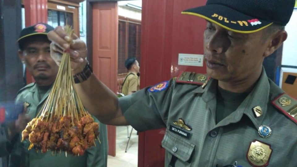 A Padang Satpol PP (Civil Service Police) officer holding up sate skewers suspected of containing pork. Photo: Humas Kota Padang / Facebook