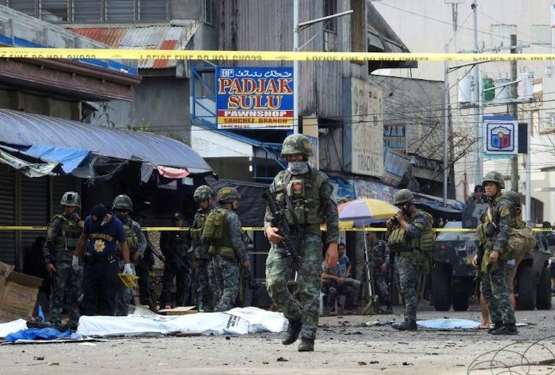 Policemen and soldiers keep watch as body bags (in white), containing the remains of blast victims, as seen in a cordoned area outside a church in Jolo, Sulu province on the southern island of Mindanao, on January 27, 2019. (Photo by NICKEE BUTLANGAN / AFP)