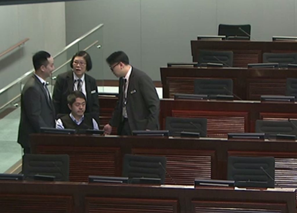 Security staff wonder how best to deal with Ted Hui Chi-fung's refusal to leave his seat at the LegCo earlier today. Screengrab via LegCo.