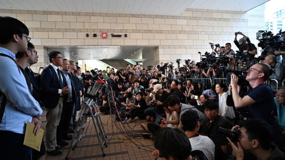 Sociology professor Chan Kin-man (third left, white shirt), law professor Benny Tai (fourth left), and other pro-democracy campaigners speak to the press outside the West Kowloon Magistrates Court today. Photo via AFP.
