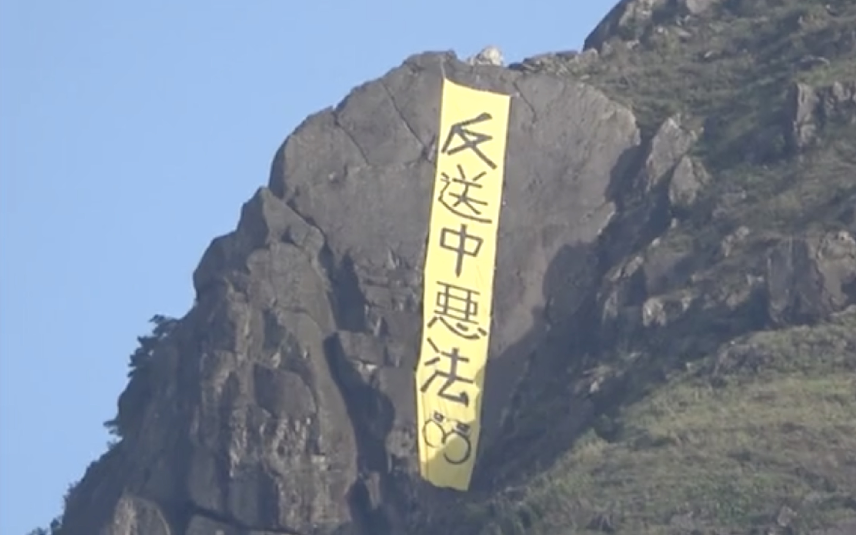 A yellow banner with the words “oppose the evil send-to-China law” was spotted hanging off the hillside of Kowloon Peak this morning. Screengrab via Apple Daily video.