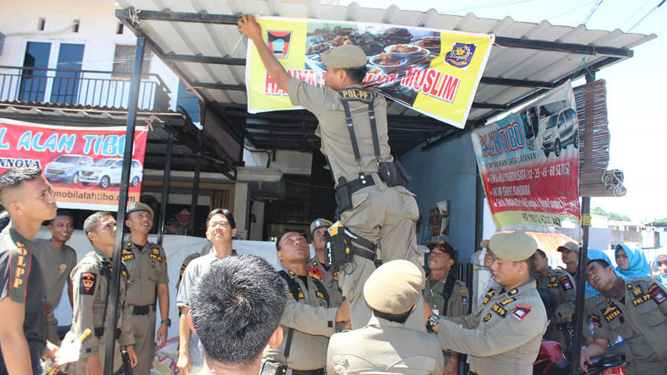 A public order officer in the Indonesian city of Padang putting up a banner saying, “Only for non-Muslims” in front of a restaurant that remained open during Ramadan. Photo: Facebook/Humas Kota Padang