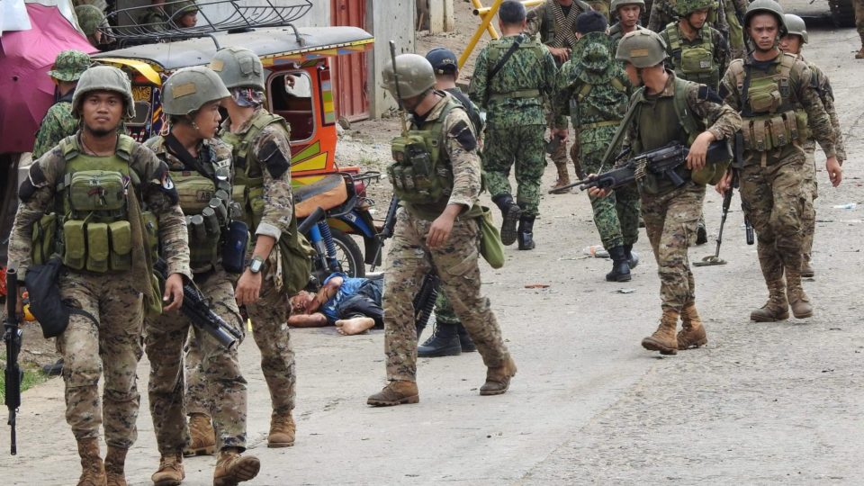 Soldiers walk past the body of a man slumped beside a tricycle following an armed attack in front of the temporary headquarters of the army’s First Brigade Combat team, in Jolo on the southern island of Mindanao on June 28, 2019. <i>Photo: Nickee Butlangan/AFP</i>