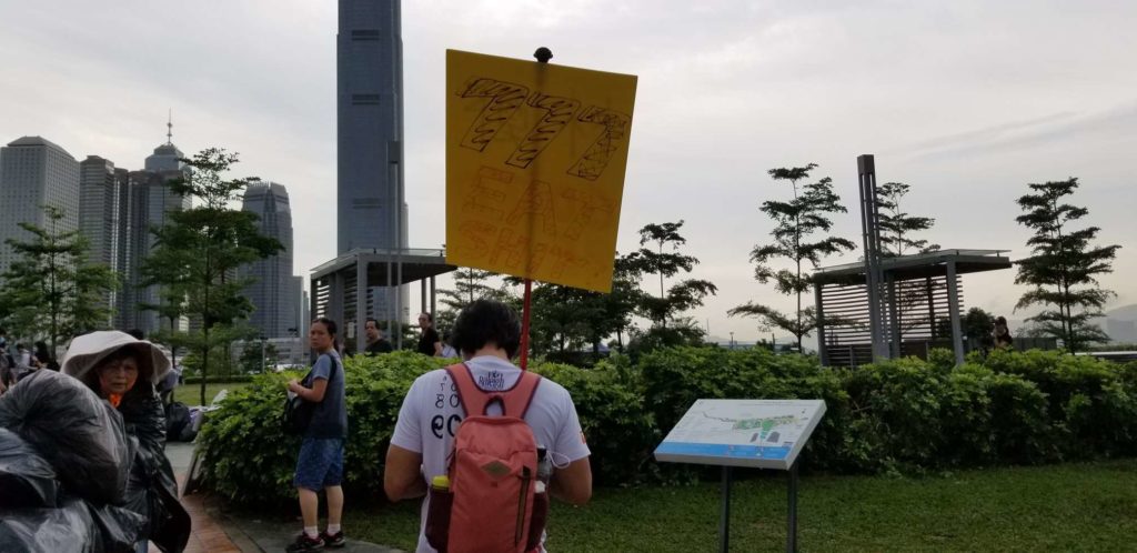 A protester in Tamar Park this morning carries a sign that reads '777 Eat Shit,' 777 being a reference to both the number of votes won by CE Carrie Lam and a homophone in Cantonese for 'dick.' Photo by Vicky Wong.