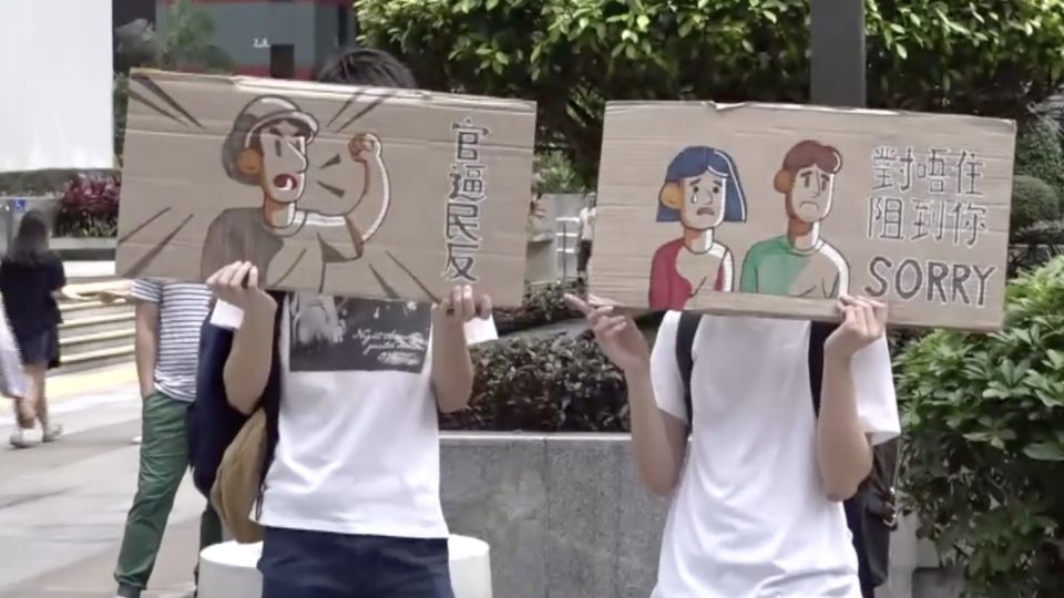 Protesters hold signs that read “The oppressive government drives people to rebel,” and “Sorry for blocking you” outside government offices today. Screengrab via Apple Daily video.