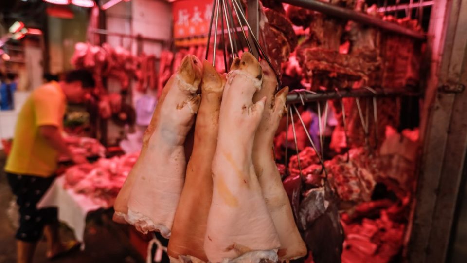 Pig trotters hang from hooks as a butcher prepares pork meat at a market in Hong Kong in May. Photo via AFP.