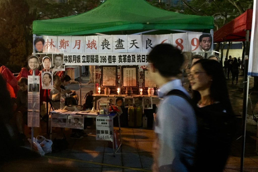 Vigil attendees walk past a stall featuring a shrine to the dead, and signs calling Hong Kong's past and current leaders 'heartless.' Photo by Stuart White.
