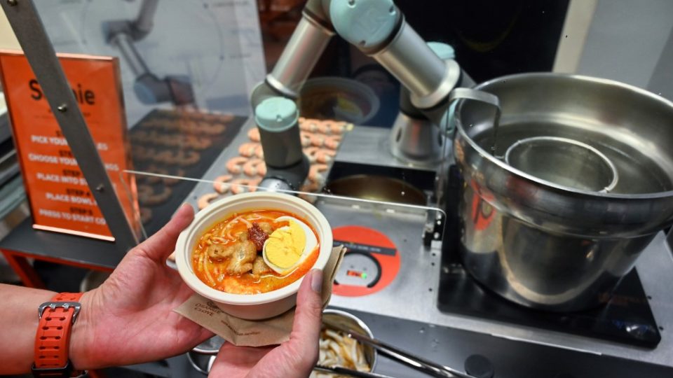 This picture taken on July 26, 2019 shows a person holding a bowl of laksa, a local dish of rice noodles served in a curry sauce, after it was prepared by Sophie the robotic chef in Singapore. (Photo by Roslan RAHMAN / AFP)