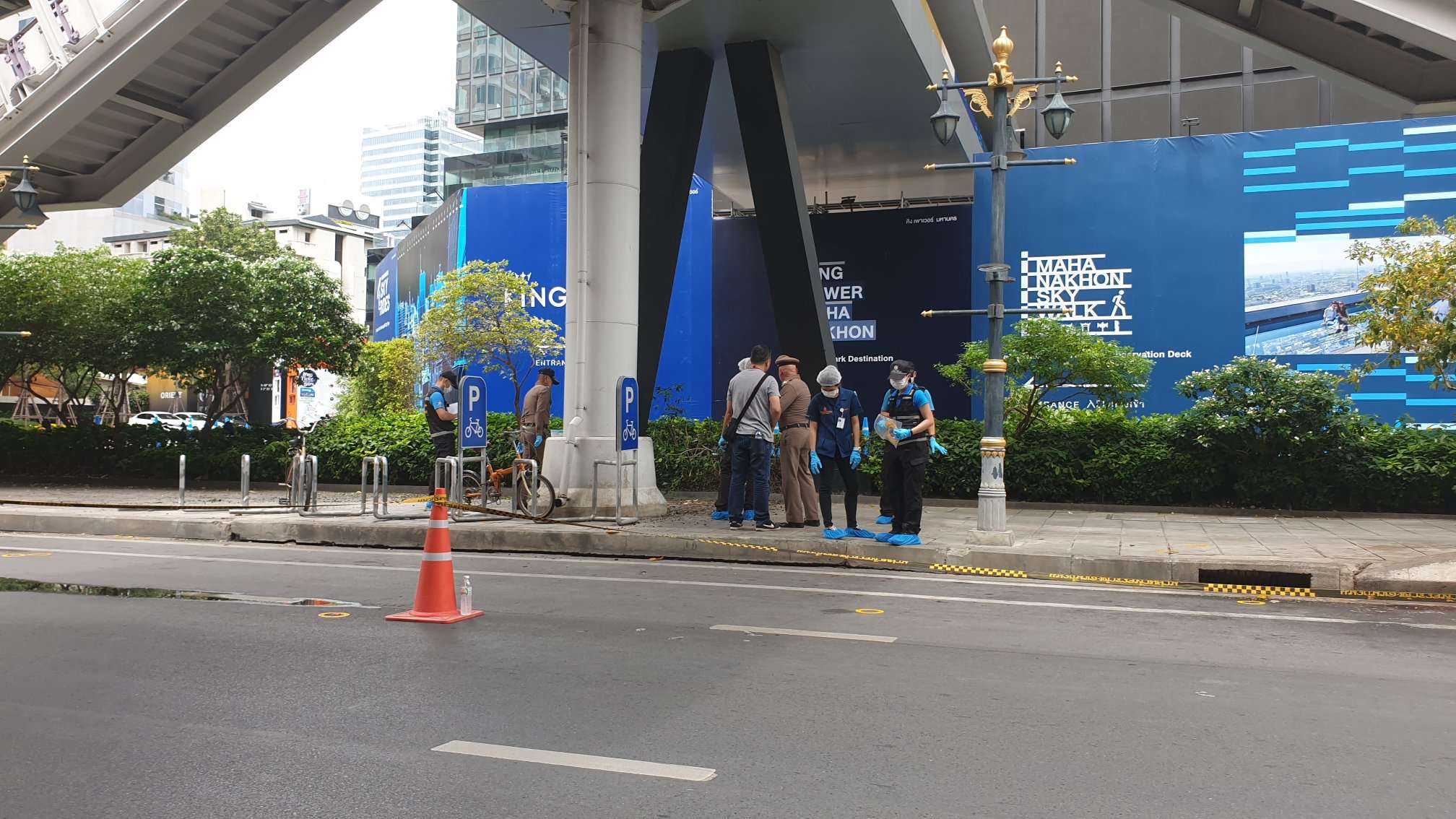 Investigators comb through bushes beneath a skywalk connecting BTS Chong Nonsi to the King Power MahaNakorn Tower in Bangkok.