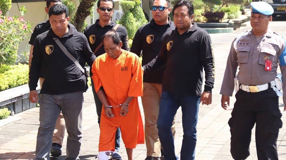 Police officers escort Wayan Soma to a press conference in Denpasar. Photo: Polresta Denpasar / Facebook 