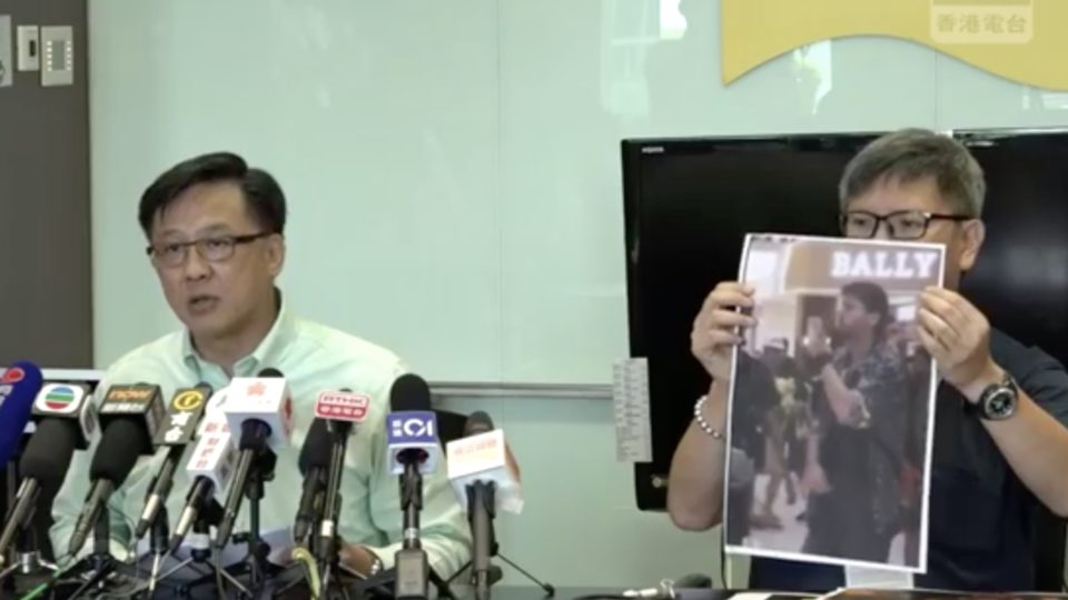 Junius Ho’s aide holds up a photo of a man they claim is a foreign commander responsible for stoking recent protests. Screengrab via Facebook/RTHK.