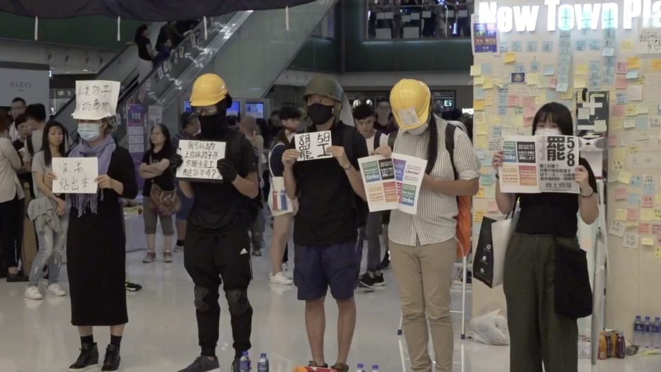 Protesters at New Town Plaza in Sha Tin last night hold up signs calling on Hongkongers to support a citywide strike on Monday. Screengrab via Facebook/Stand News.