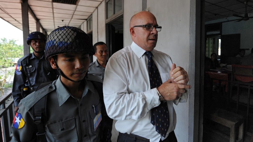 In this file photo taken on March 23, 2011, Australia’s Ross Dunkley, co-founder of the Myanmar Times newspaper, is escorted by Myanmar policeman as he arrives for a hearing at the Kamaryut township court in Yangon. Photo by Soe Than Win / AFP