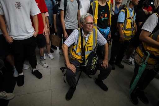 This picture taken on September 7, 2019 shows “Grandpa Wong” (C), 85, taking a rest on a portable stool set up in between a group of protesters in the Tung Chung district in Hong Kong. – Despite his age, Wong is a regular sight at Hong Kong’s street battles, hobbling towards police lines, placing himself in between riot officers and hardcore protesters, hoping to de-escalate what have now become near daily clashes. (Photo by VIVEK PRAKASH / AFP)