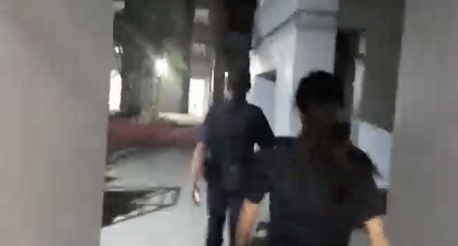 Police officers heading towards their car as a woman records them on video from behind. 