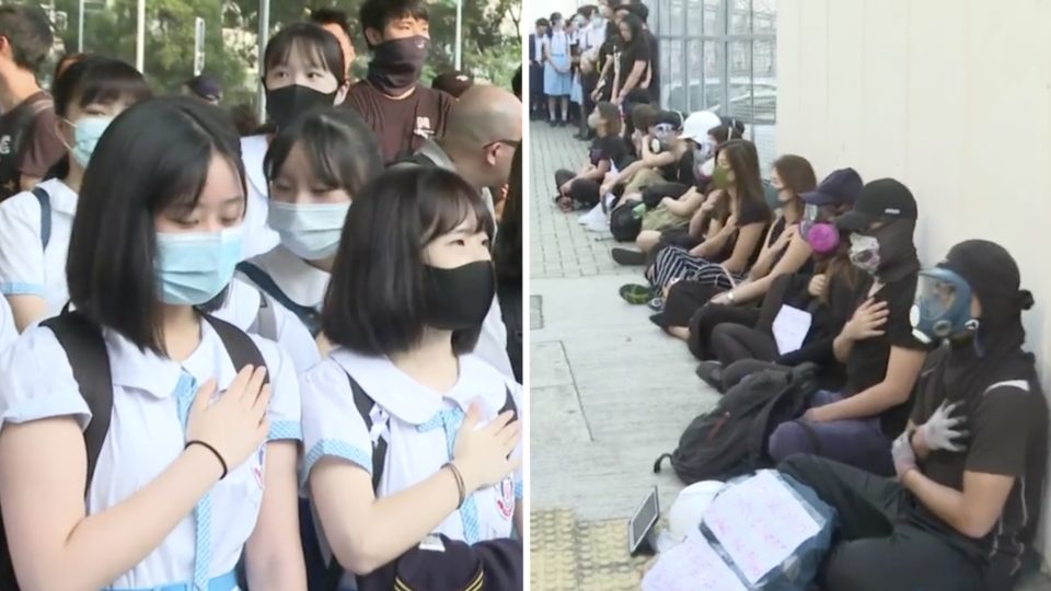 People gathered outside a Tsuen Wan high school place their hand on their chest in solidarity with a student who was shot in the chest at close range by a police officer during yesterday’s National Day protests. Screengrab via Facebook/RTHKRTHK 