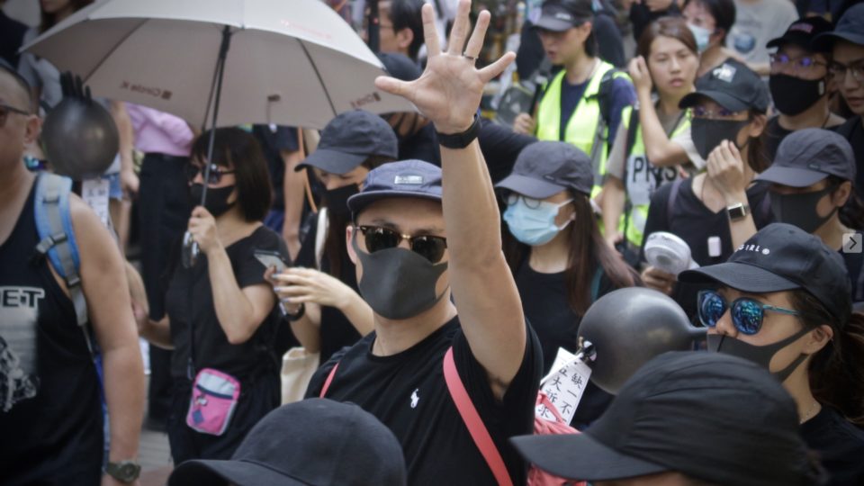 A masked protester holds up five fingers, the gesture used to represent the slogan ‘five demands, not one less.’ Photo by Vicky Wong.