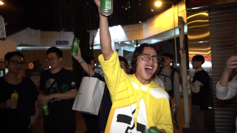 A man raises a beer with others in Tuen Mun after controversial politician Junius Ho loses his district council re-election bid last night. Screengrab via YouTube.