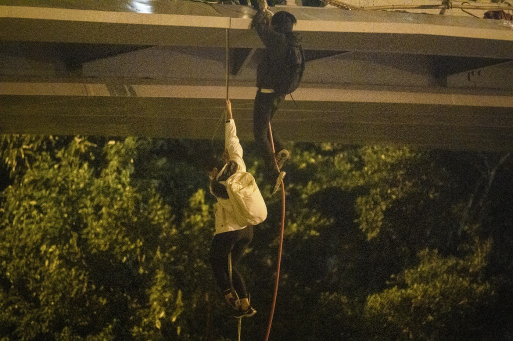 Protesters lower themselves down a rope from a bridge to a highway to escape from Hong Kong Polytechnic University campus and from police on Nov. 18, 2019. Photo via AFP.