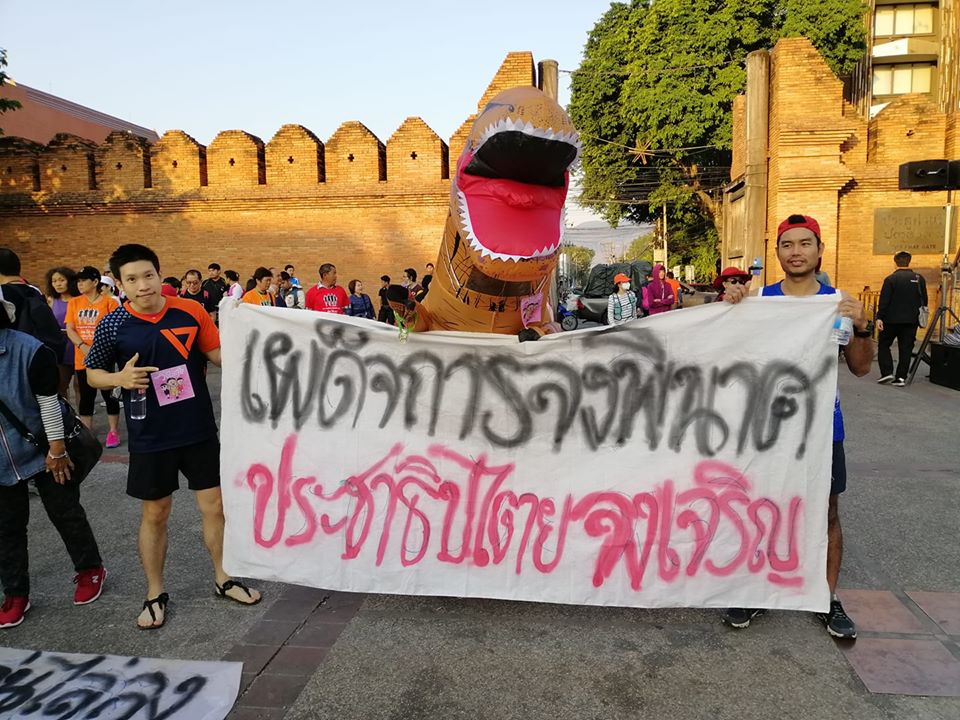 Runners and a dinosaur – a common stand-in for the old guard – raise a banner reading ‘May dictatorship destroyed. Long live democracy’ during the Run Against Dictatorship on Jan. 12 in Chiang Mai. Photo: Witchakorn Wanasanwongkot / Courtesy