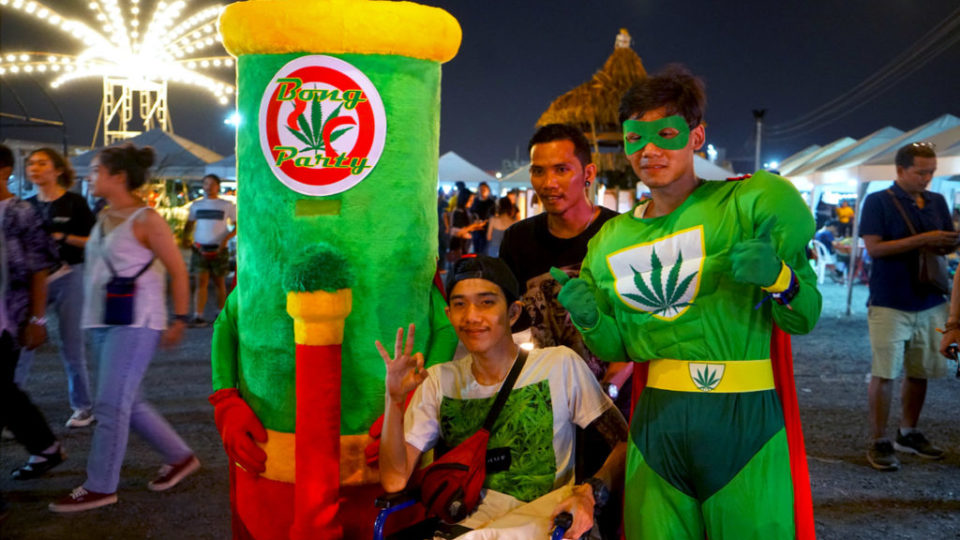 A young man in a wheelchair poses with a human bong mascot and Super Weedman at a 2019 cannabis festival at the Runway 3119 Night Market in Bangkok.
