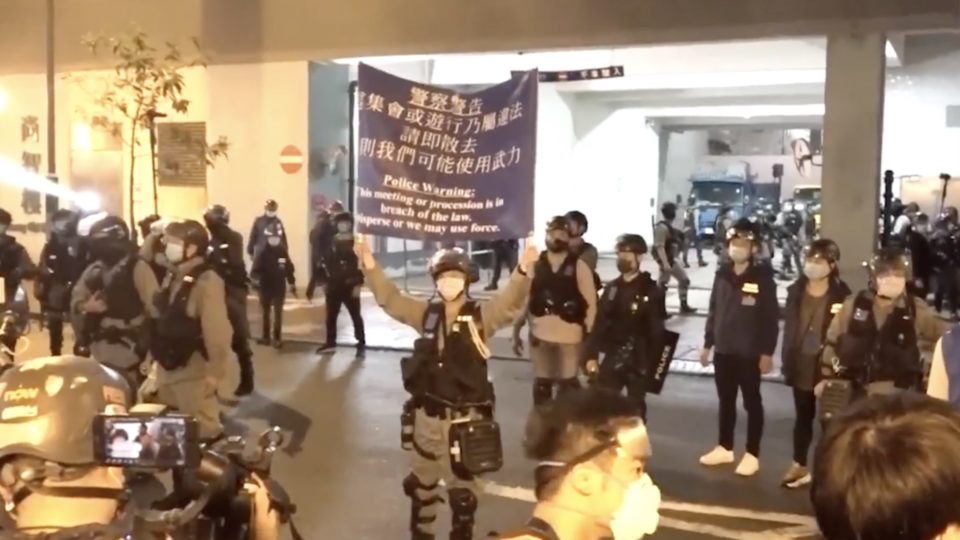 Riot police raise a blue banner declaring the gathering an illegal assembly. Screengrab via Facebook video/RTHK.